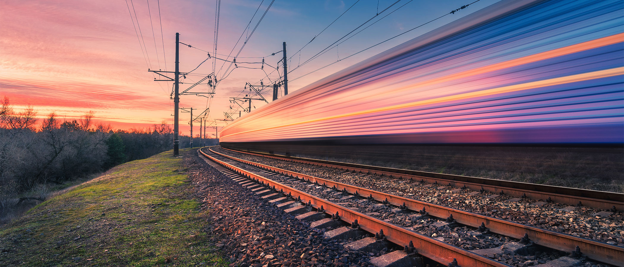 Fast-moving electric train on rural tracks at sunset.