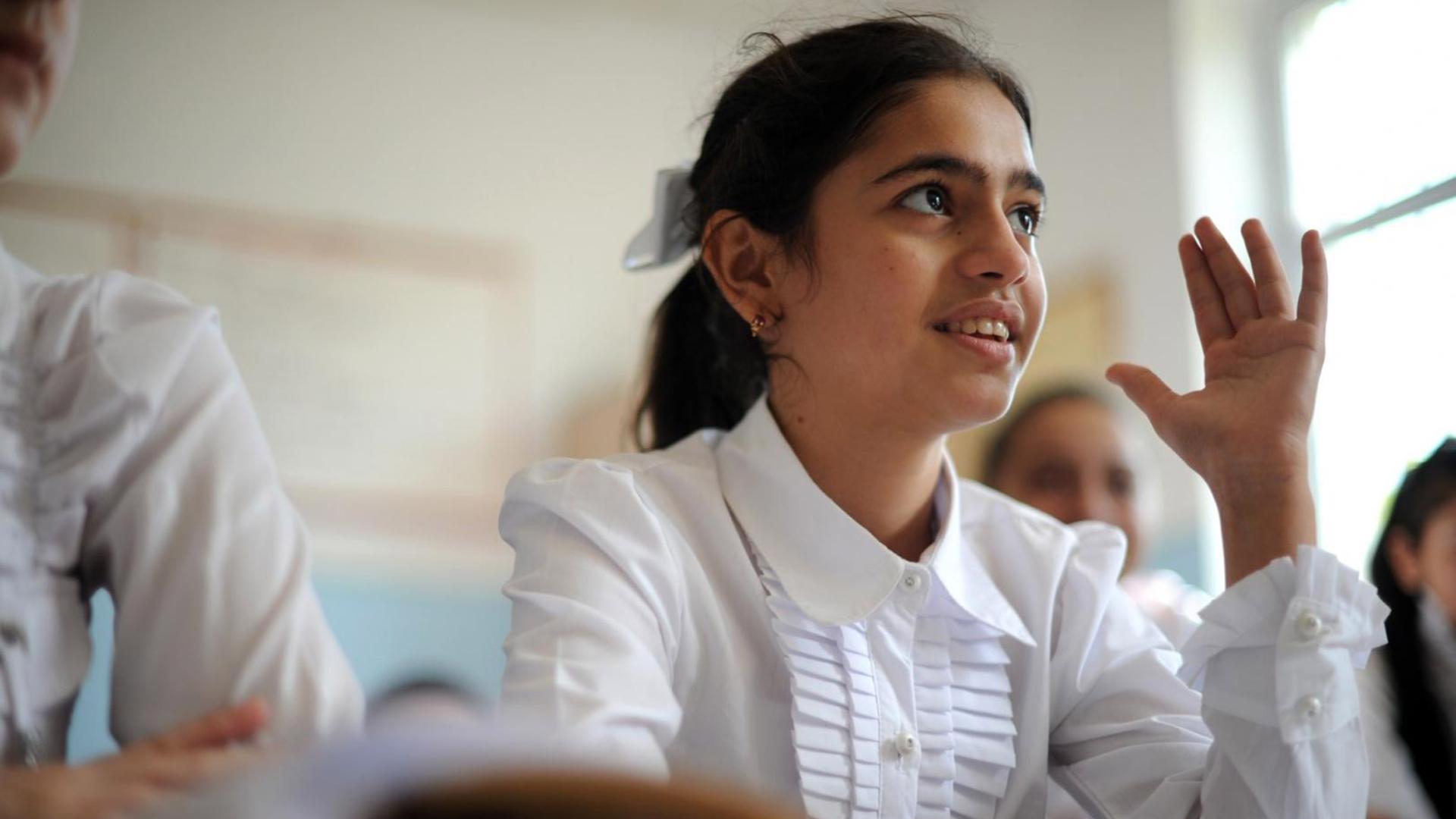 Young female student raising hand in classroom.