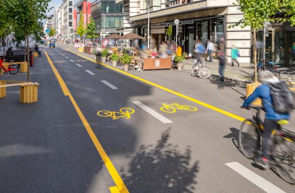 Commuter riding a bicycle in a two-direction bike lane on a pedestrian-friendly street in the shopping district of a downtown area.
